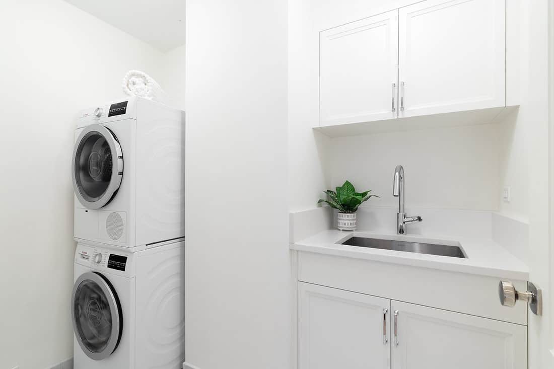 A clean laundry room with white cabinets, a utility sink, granite countertop, and Bosch washer and dryer appliances