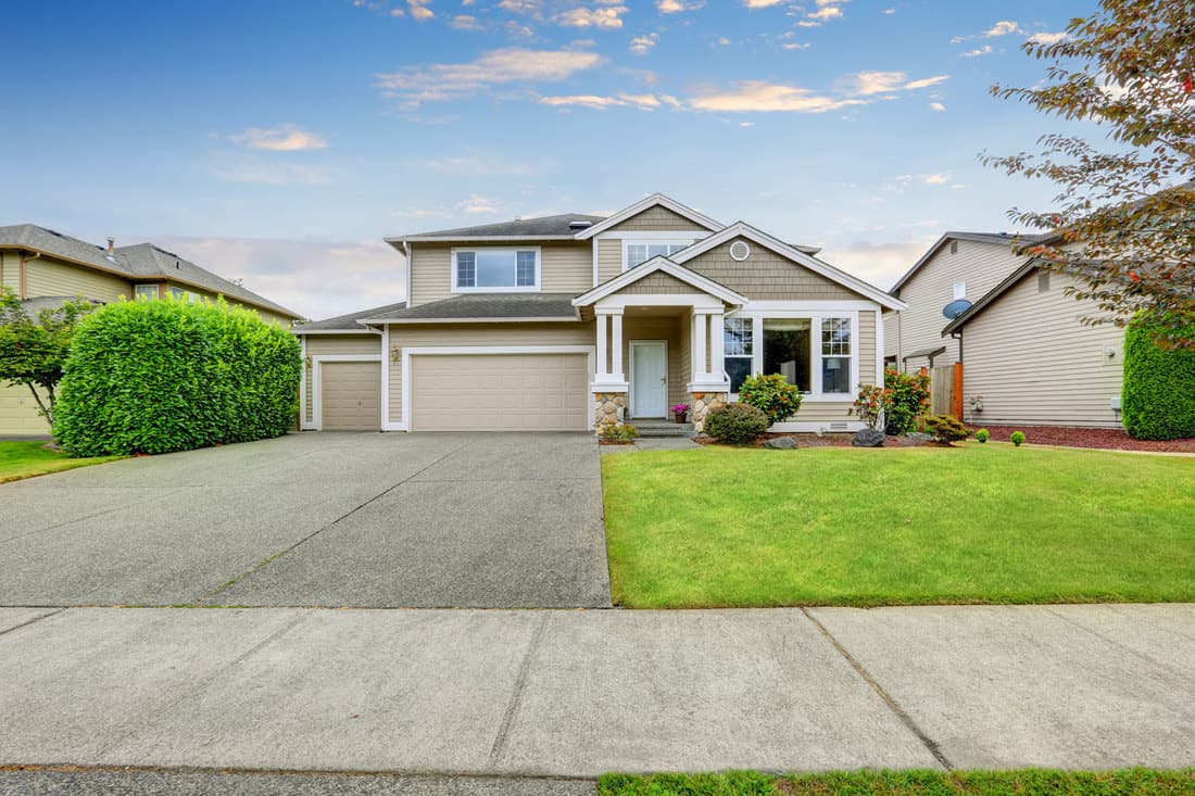A gorgeous two storey American home with a huge driveway and a newly mowed lawn, How Thick Should A Concrete Driveway Be?