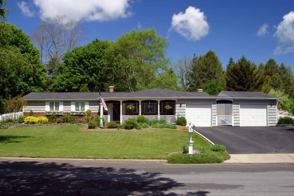 A long ranch-style house with light gray painted sidings, white painted garage doors, and an asphalt driveway