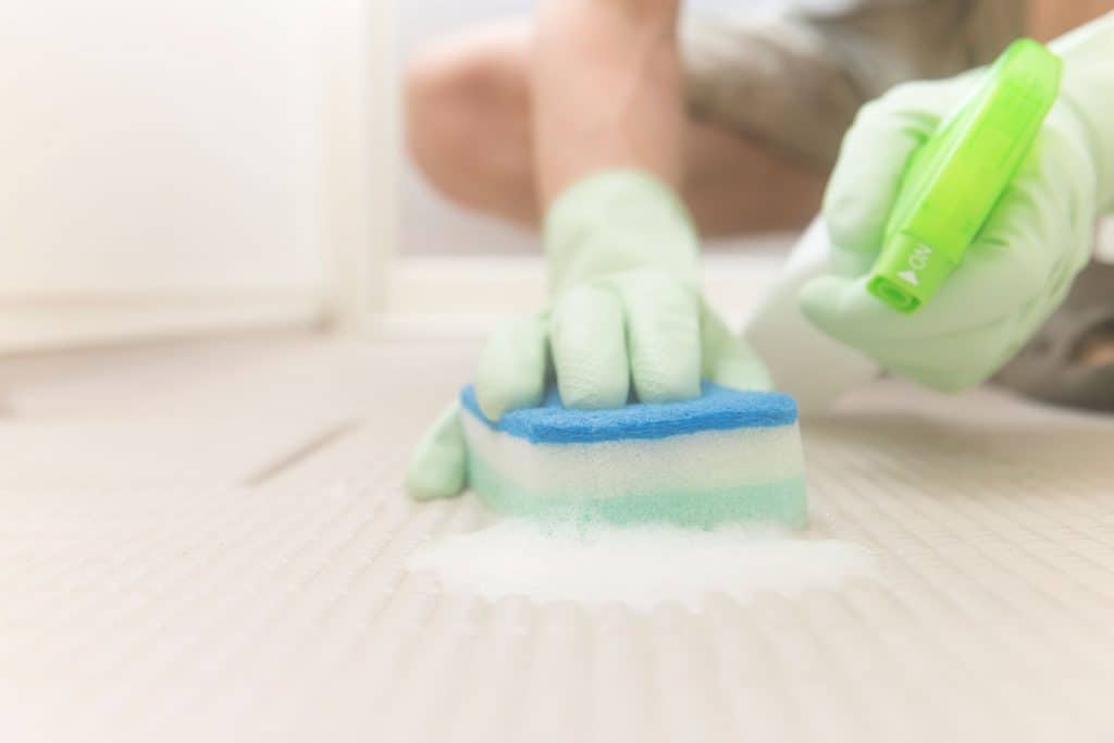 A man cleaning the bathroom floor using a spray and sponge