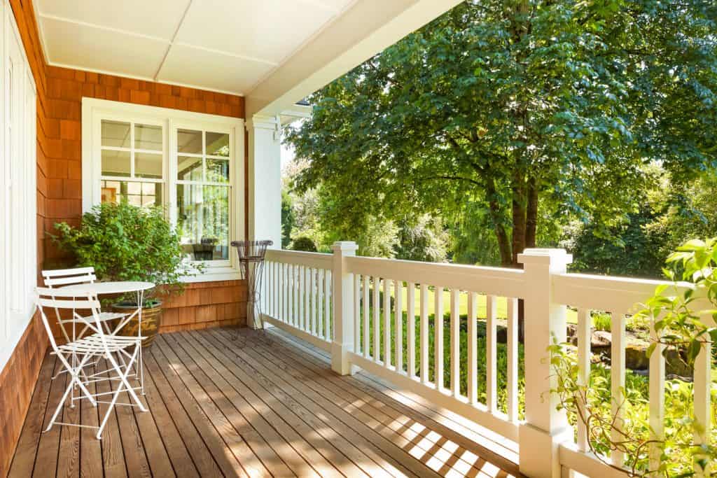 Un porche spacieux et d'inspiration rustique avec des revêtements en bardeaux de bois bruns, une clôture avant peinte en blanc et un plancher en bois