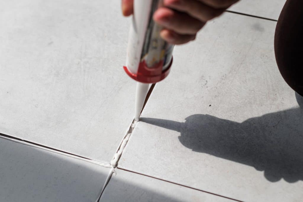 A tile setter putting grout using a caulking gun between tiles for water protection