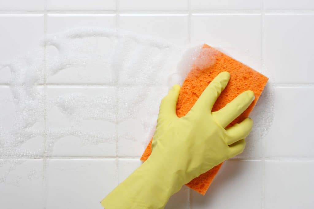 Eine Frau, die Handschuhe und einen Schwamm trägt, um die Fliesen des Badezimmers zu reinigen