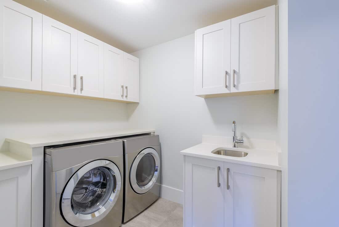 An empty laundry room with cabinet, sink, washer and drier