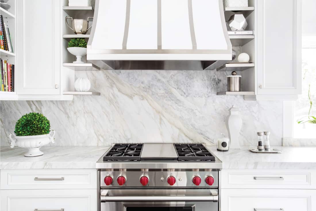 Bright horizontal image of classic white kitchen, with gas range and Sleek Matching Marble backsplash