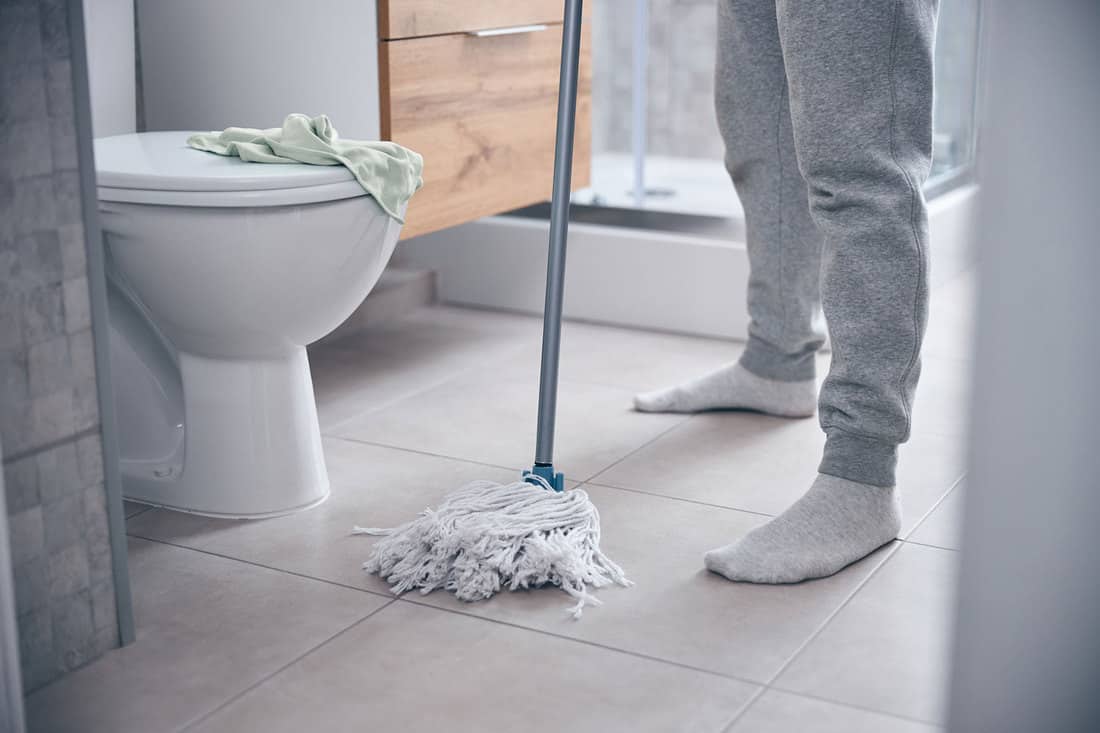 Cropped photo of a modern man standing on the floor at a ceramic toilet bowl mopped the bathroom floor, How Often Should You Mop The Bathroom Floor?