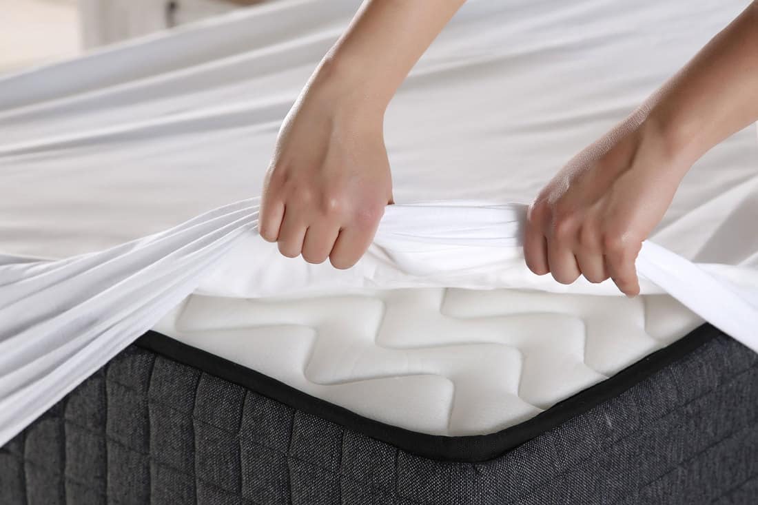 Female hand pulling mattress cover white sheets, Can Mattress Covers Make You Sweat?