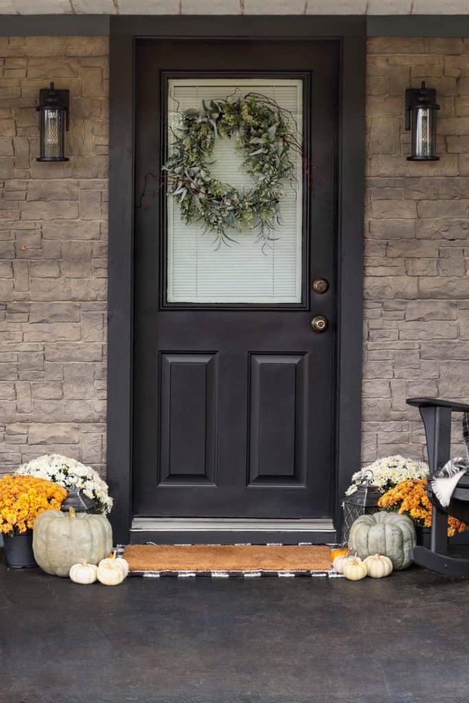 Porche décoré pour le jour de Thanksgiving avec une couronne maison accrochée à la porte.  Courges anciennes, citrouilles blanches et chrysanthèmes créant une atmosphère invitante.