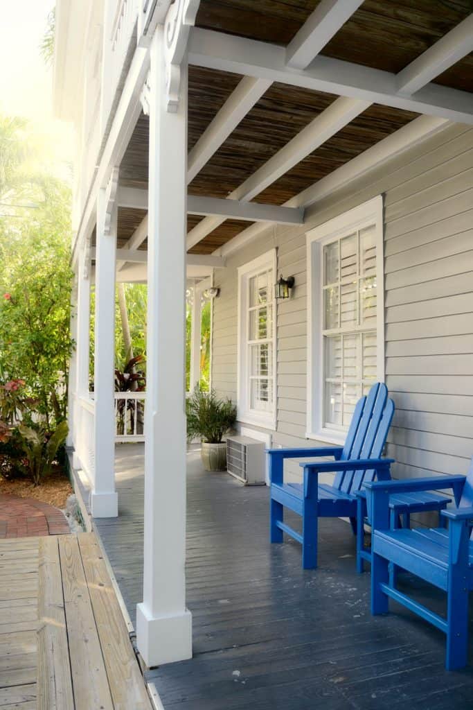 Front porch of a house with blue chairs, wooden sidings, and contrasting beams