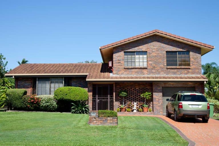Front view of a tidy split level brown brick family home with green grass and car in driveway, Do Split Level Houses Have Basements?