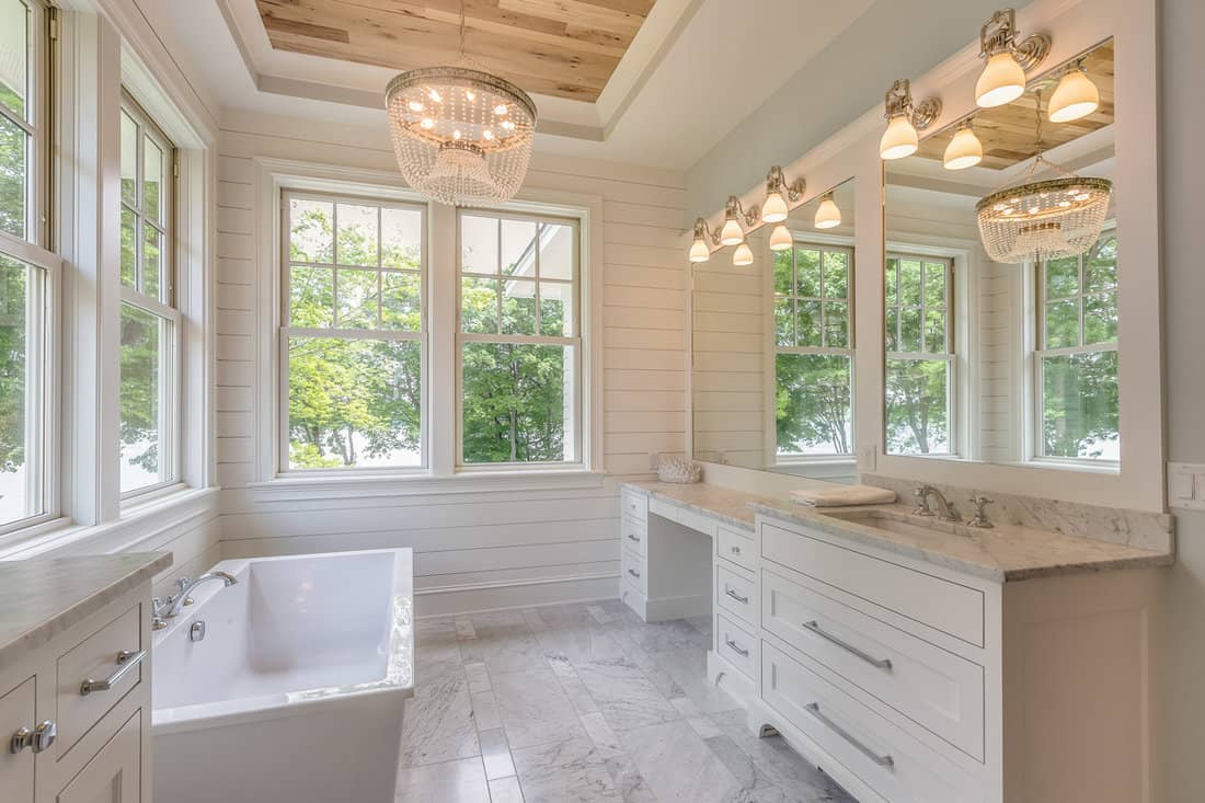 Gorgeous master bathroom with wood tray ceiling and huge white framed windows with a huge white bathtub