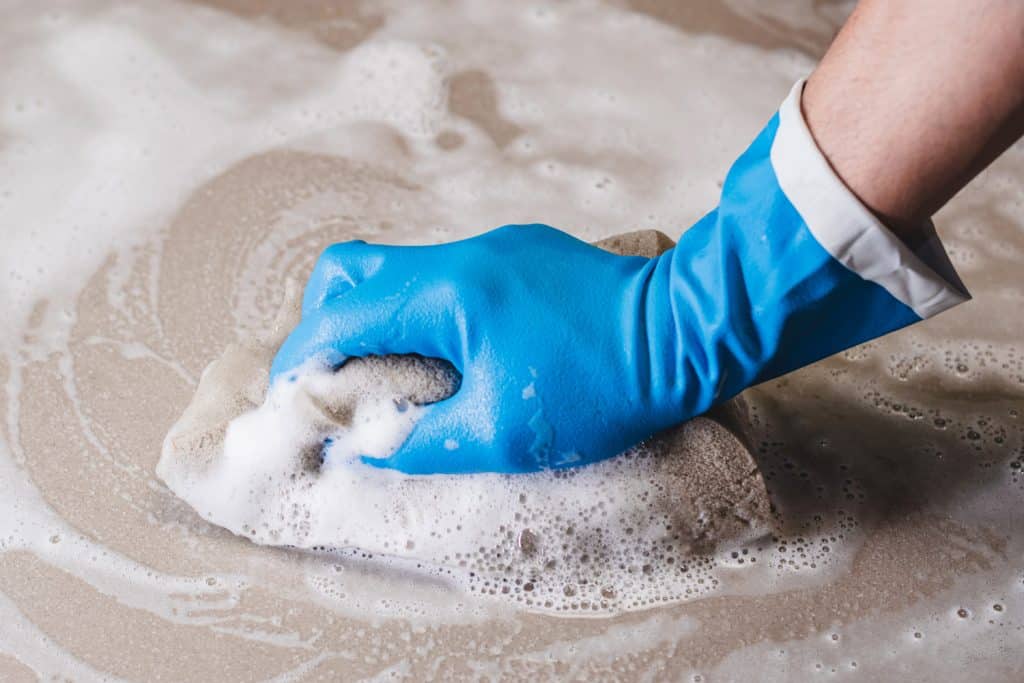 La main d'un homme portant des gants en caoutchouc bleu utilise une éponge pour nettoyer le carrelage.