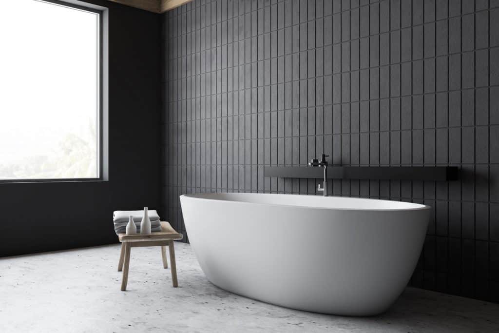 Interior of a gorgeous contemporary bathroom with a huge white bathtub and a small wooden bathroom chair on the side