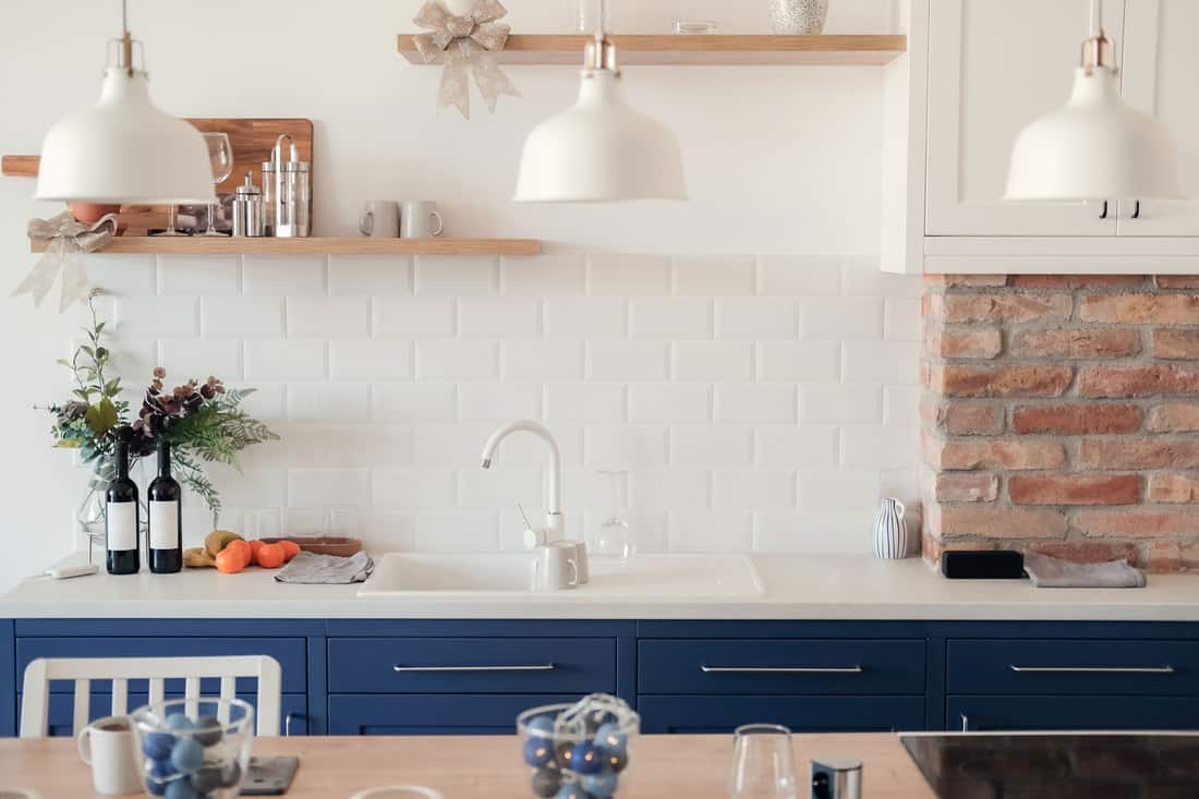 Interior of a modern kitchen with white painted backsplash blue painted kitchen cabinets and three dangling lamps, Does Backsplash Need Trim Or Edging?
