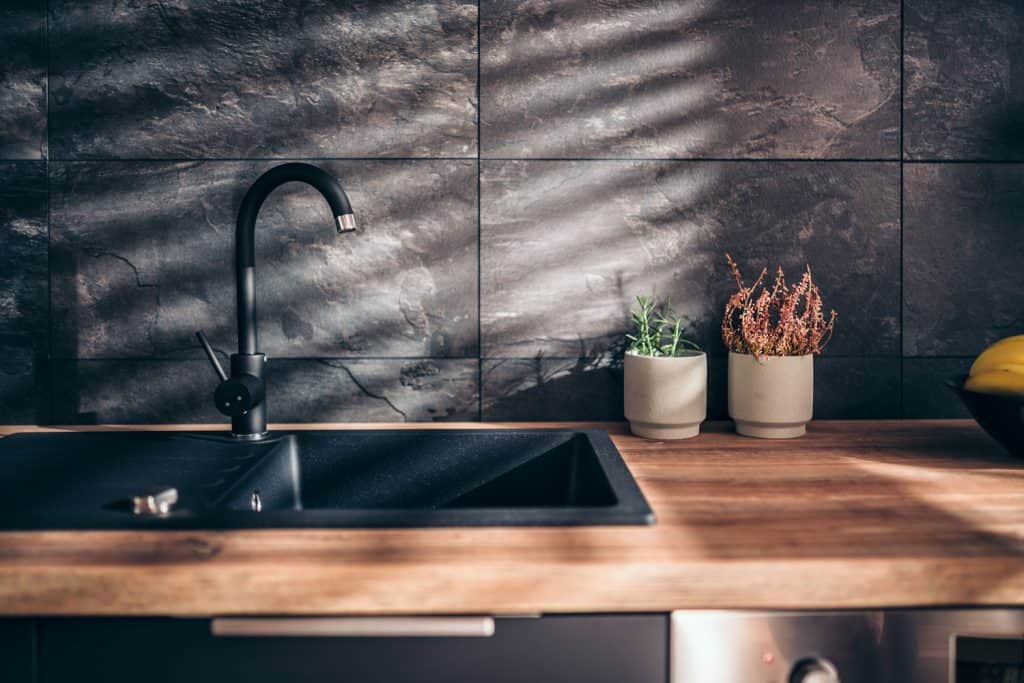 Interior of an ultra modern kitchen area with a wooden countertop and a black colored sink