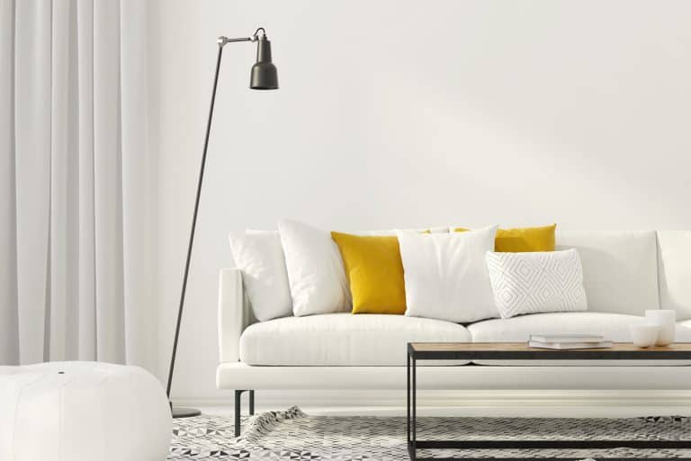 Interior of an ultra modern living room with a white painted wall, tall gray floor lamp, and a long white sofa with white and yellow throw pillows, How Tall Should A Living Room Floor Lamp Be?
