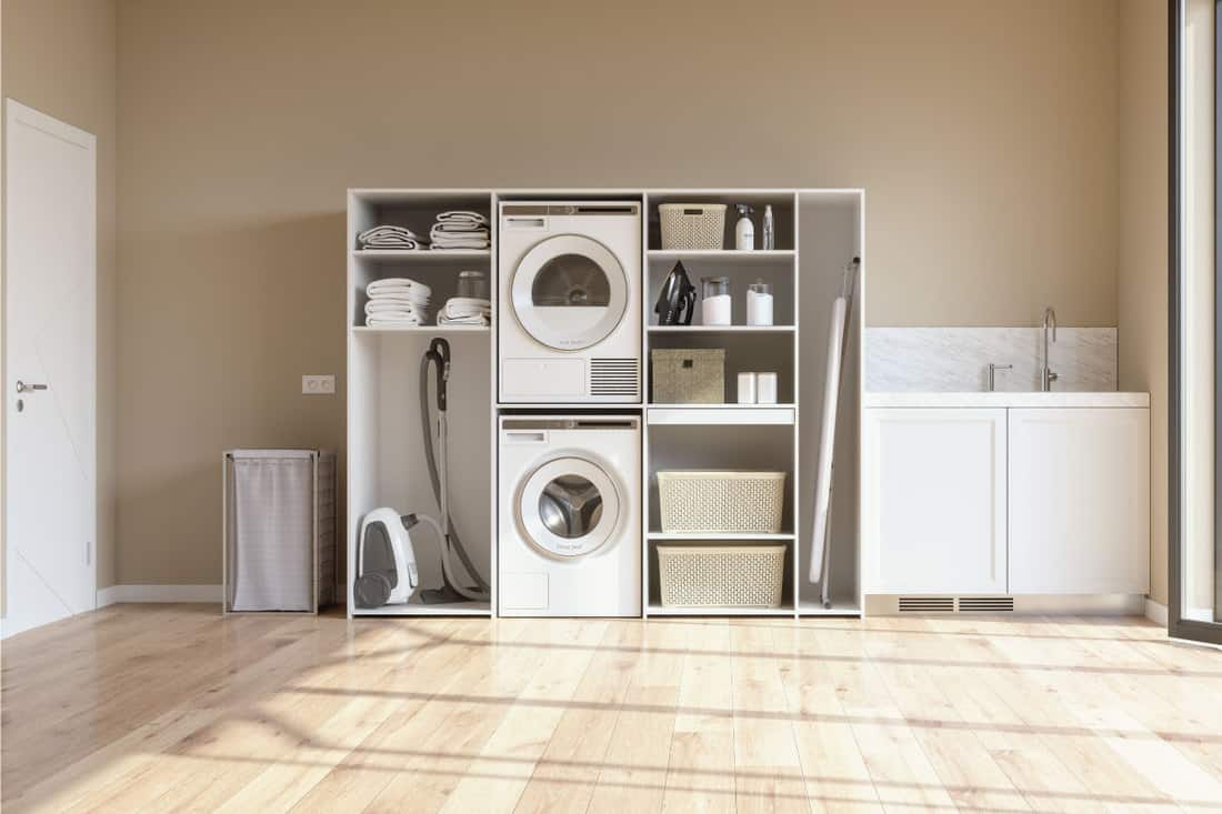 Laundry Room With Beige Wall And Parquet Floor With Washing Machine, Dryer, Laundry Basket And Folded Towels In The Cabinet. Laminate floor. What Is The Best Flooring For A Laundry Room
