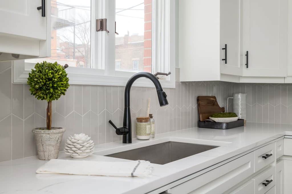 Light gray kitchen with white countertop and patterned backsplash with a metal framed window