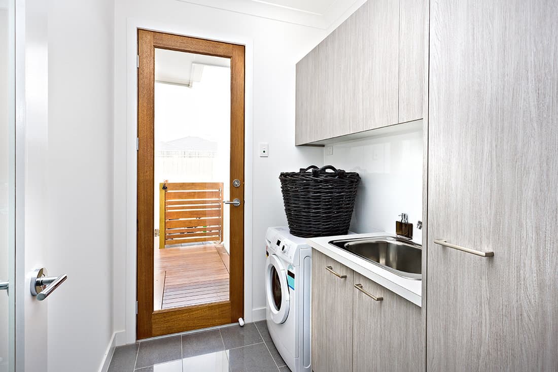 Modern laundry room with grey cupboards on the wall near a wooden door with a glass panel closed