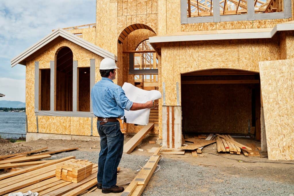 Photo d'un ouvrier du bâtiment examinant un ensemble de plans de construction sur un chantier de construction.