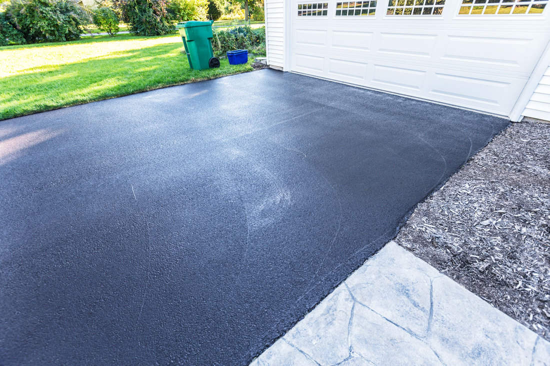 Photo of an asphalt driveway with a huge white painted garage door, How Long Does An Asphalt Driveway Last?