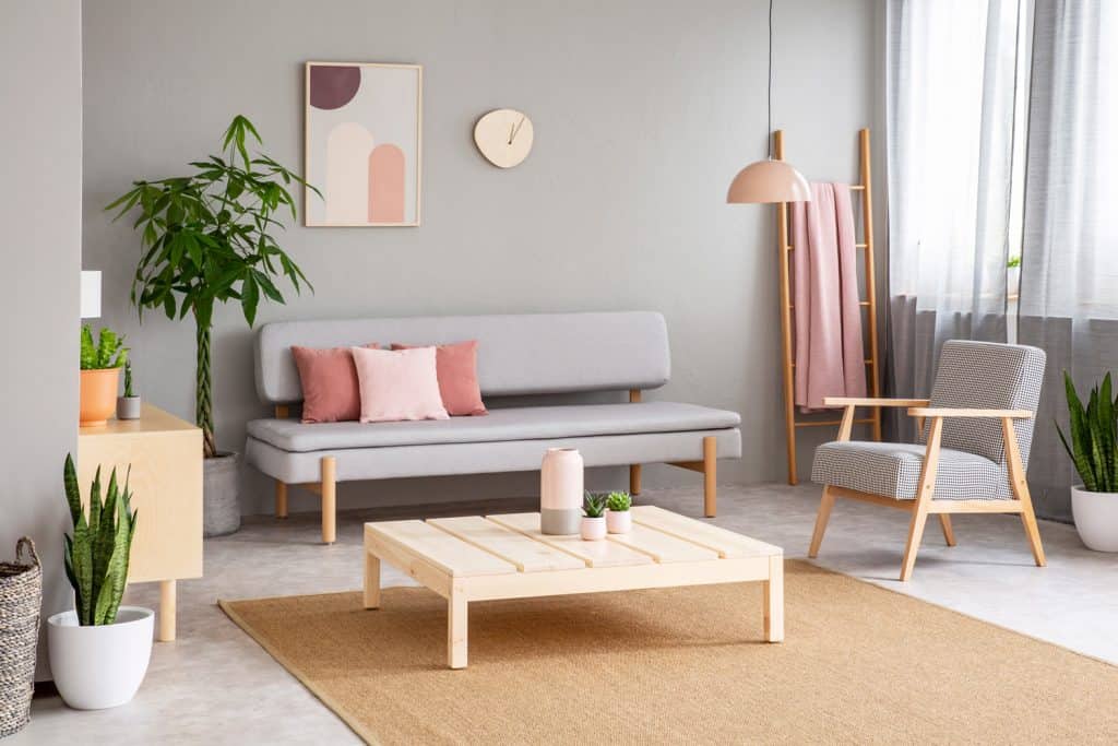 Poster and plant in living room interior with armchair next to grey sofa and wooden table. Real photo