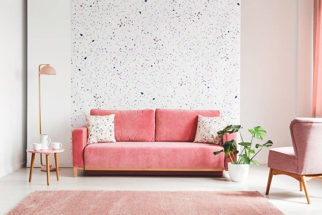 Real photo of a pink, velvet sofa, plant, coffee table with pot and cups on a lastrico wall a living room interior