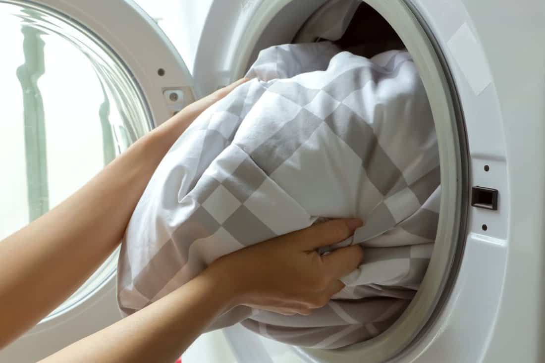 Woman loading blanket in to washing machine.