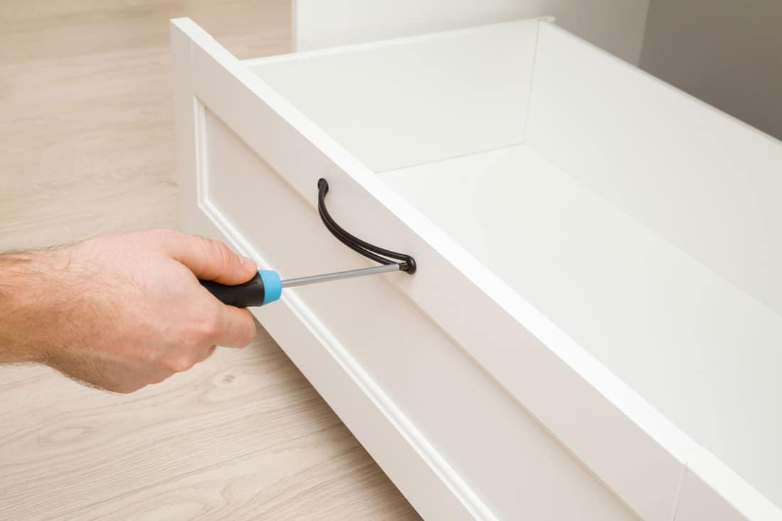 Young adult man hand using manual screwdriver and screwing black metal drawer handle