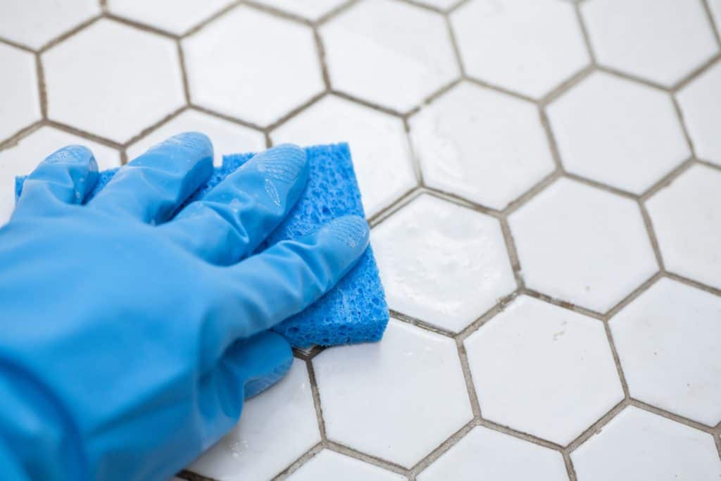 une personne portant des gants bleus tient une éponge nettoyant un sol en carrelage blanc