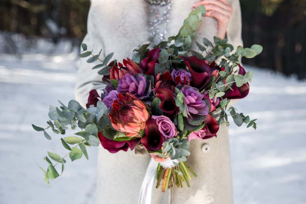 A bride holding a gorgeous array of red and violet roses