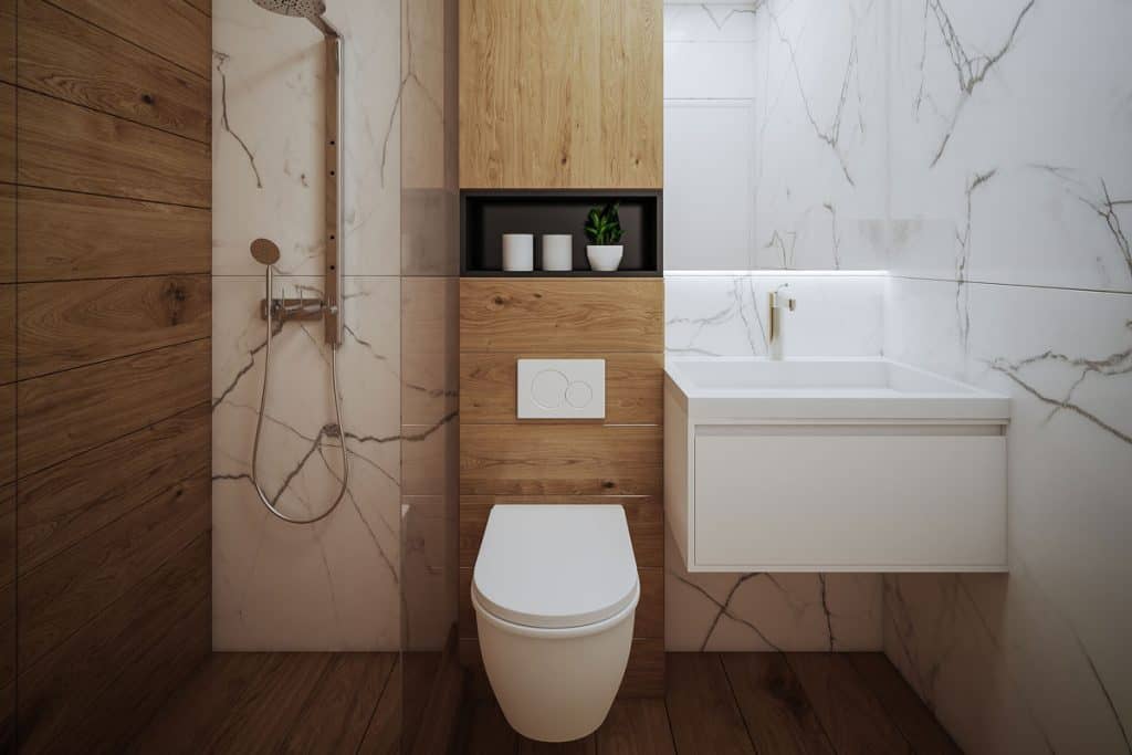 A glass walled shower area with wooden flooring and matched with marble walls