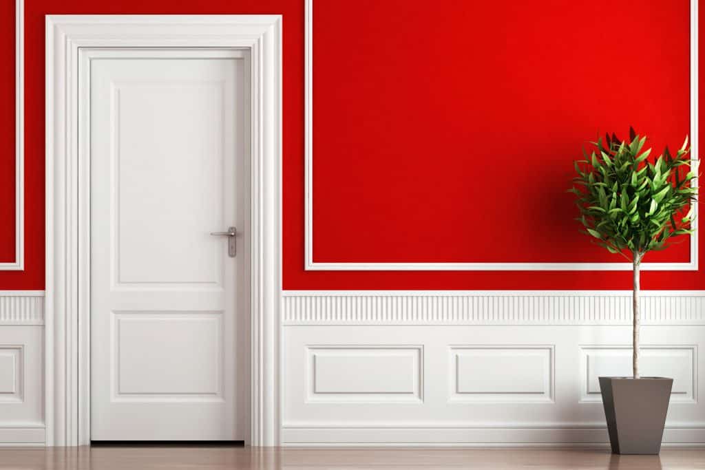 A gorgeous red painted wall with a white door, white baseboard, and a red painted wall