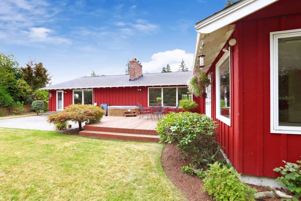 A long span bent red painted wooden sidings, ranch house with glass windows, and a gorgeous garden