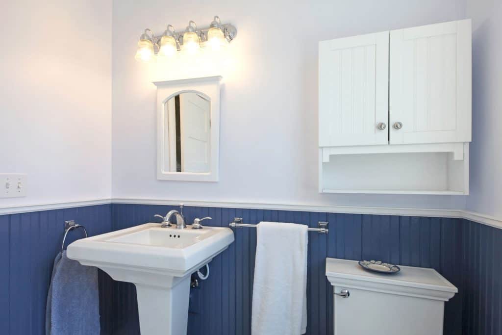 A nautical inspired bathroom with blue baseboard, tall lavatory, and a small white colored hanging cabinet