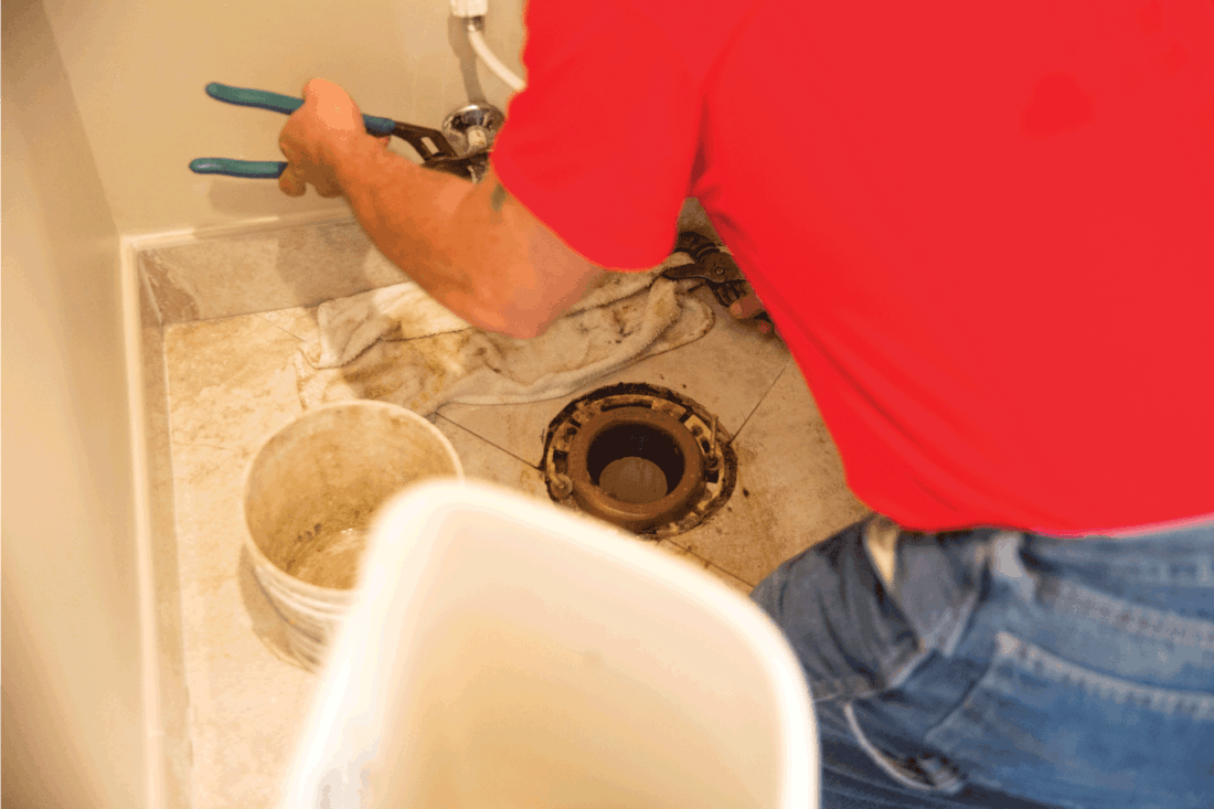 A plumber is working on repairing a toilet in a home. He is taking apart the toilet so he can replace the toilet flange.