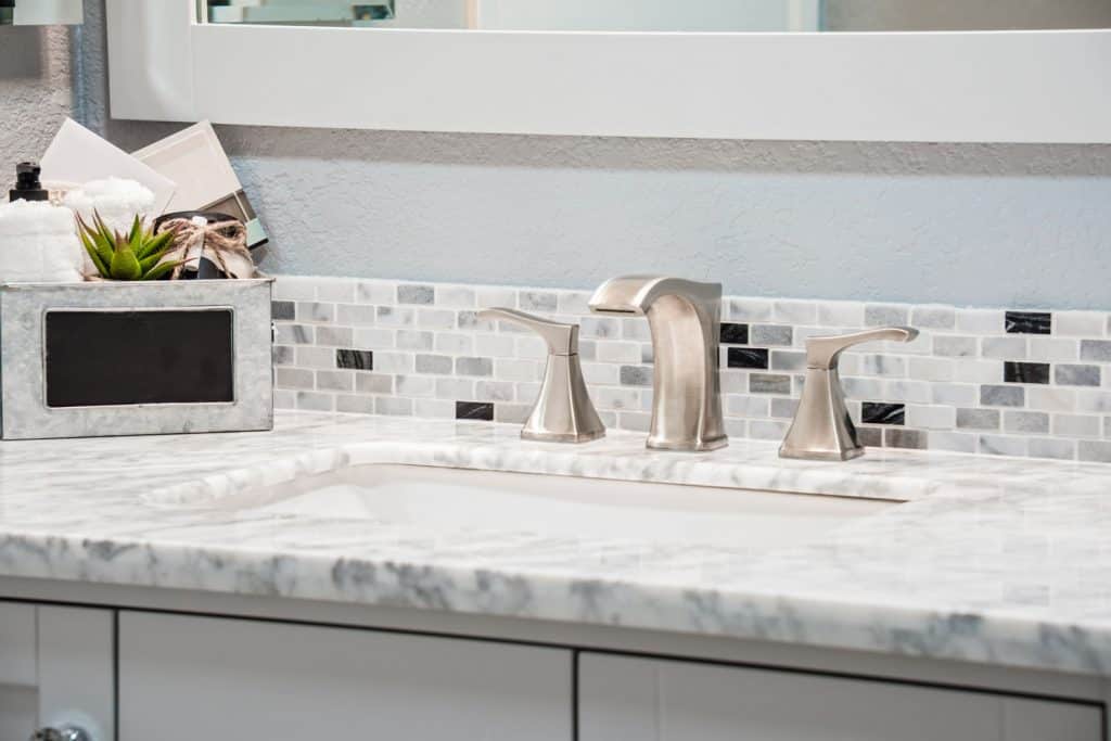 A small contemporary styled bathroom vanity with small tiled backsplash, modern faucet, and granite countertop
