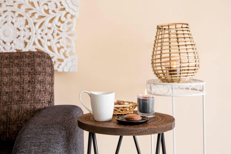 A small round end table on the side of a brown sectional sofa and a small rattan lamp on the back, 11 Great End Tables With Storage For Your Living Room