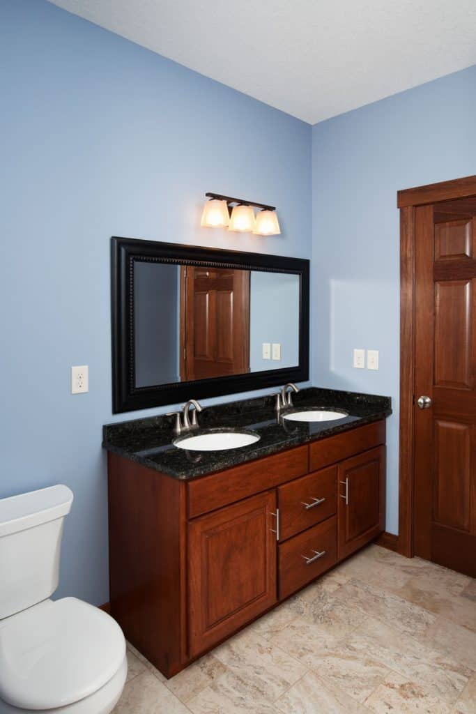A small rustic designed bathroom vanity with wooden cabinets and a dark framed rectangular mirror
