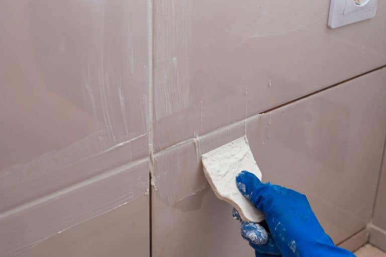 A tile setter putting grout on the tiles of bathroom, How Long Does Bathroom Grout Take To Dry?