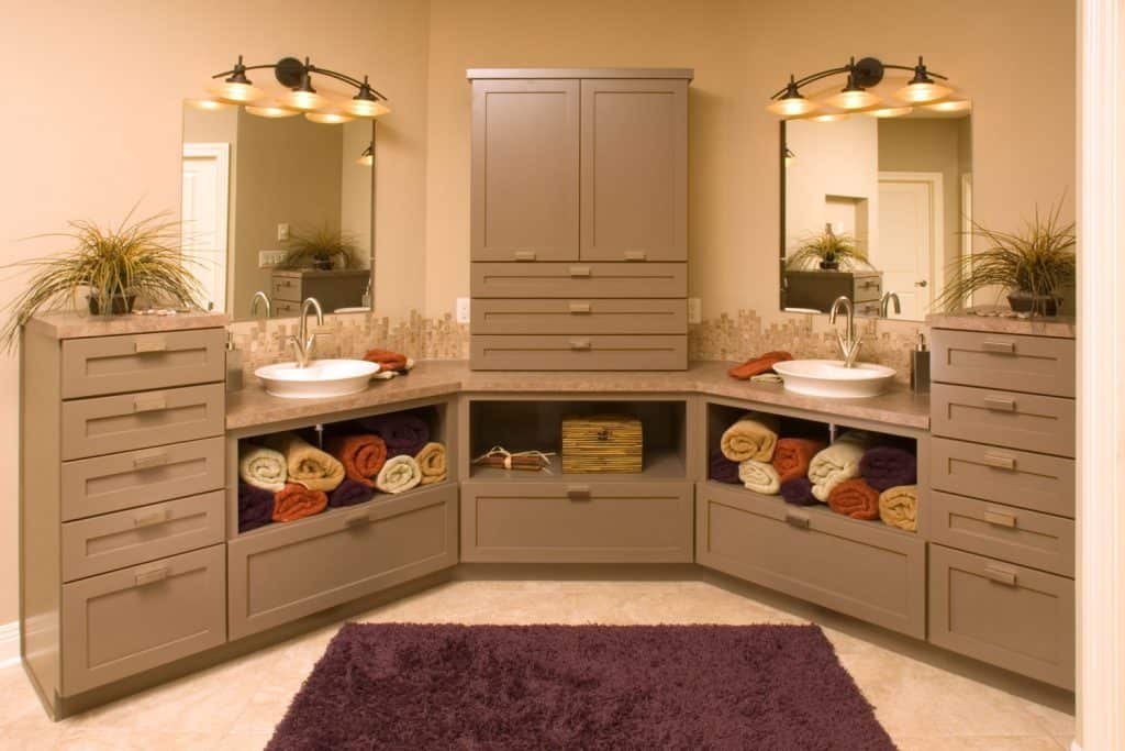 A wide cabinet design painted in light brown with rolled up bath towels on the dividers