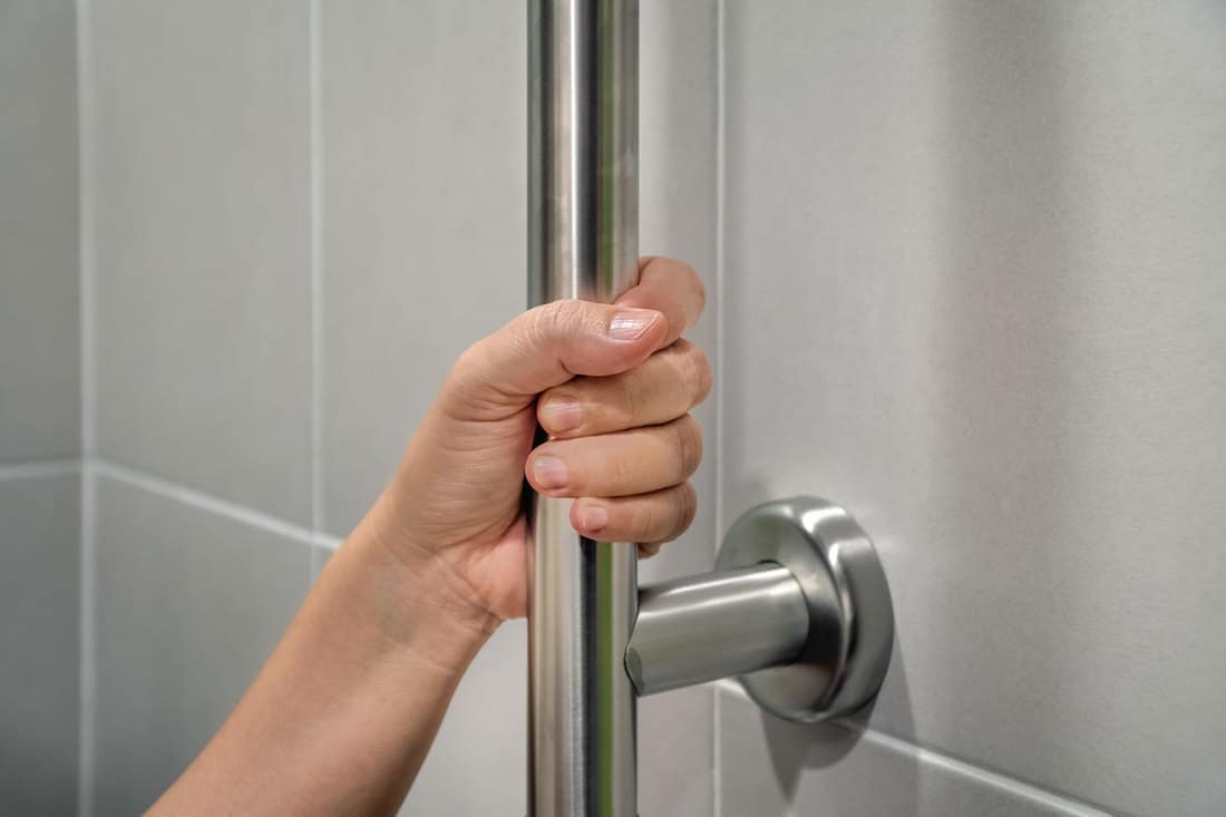 A woman holding a grab bar inside the bathroom, Do Grab Bars Need To Be Installed Into Studs?