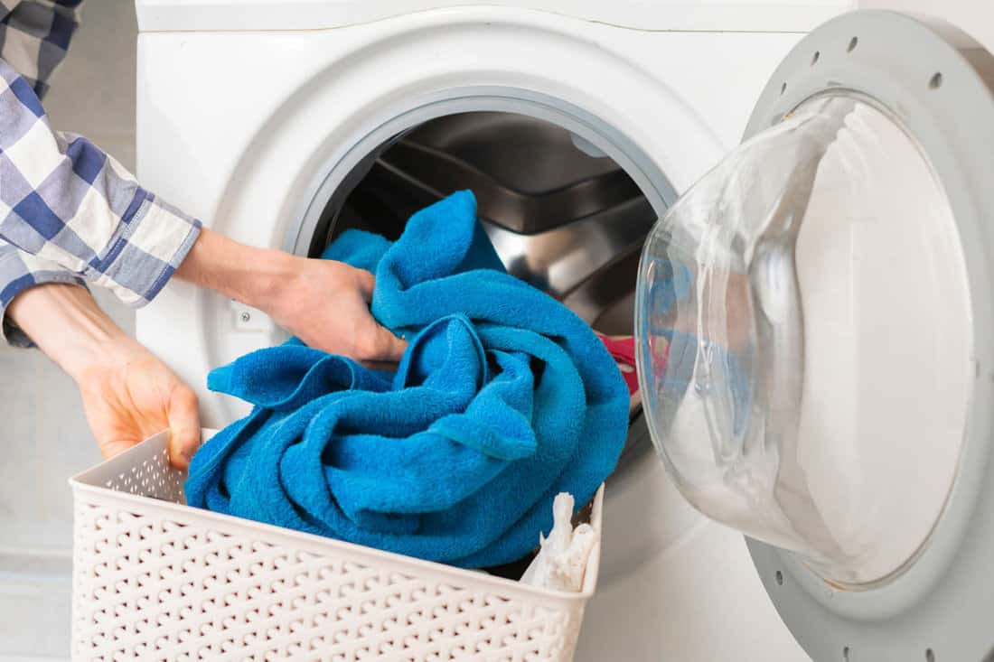 A woman putting a blue towel to a washing machine for a laundry