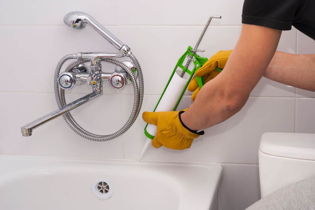 A worker applying caulk to the bathroom sink, Can You Caulk Over Grout In The Bathroom?