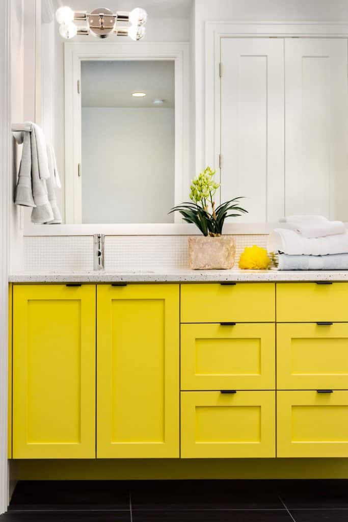 A yellow cabinet in the vanity with a huge mirror and a small plant placed on top