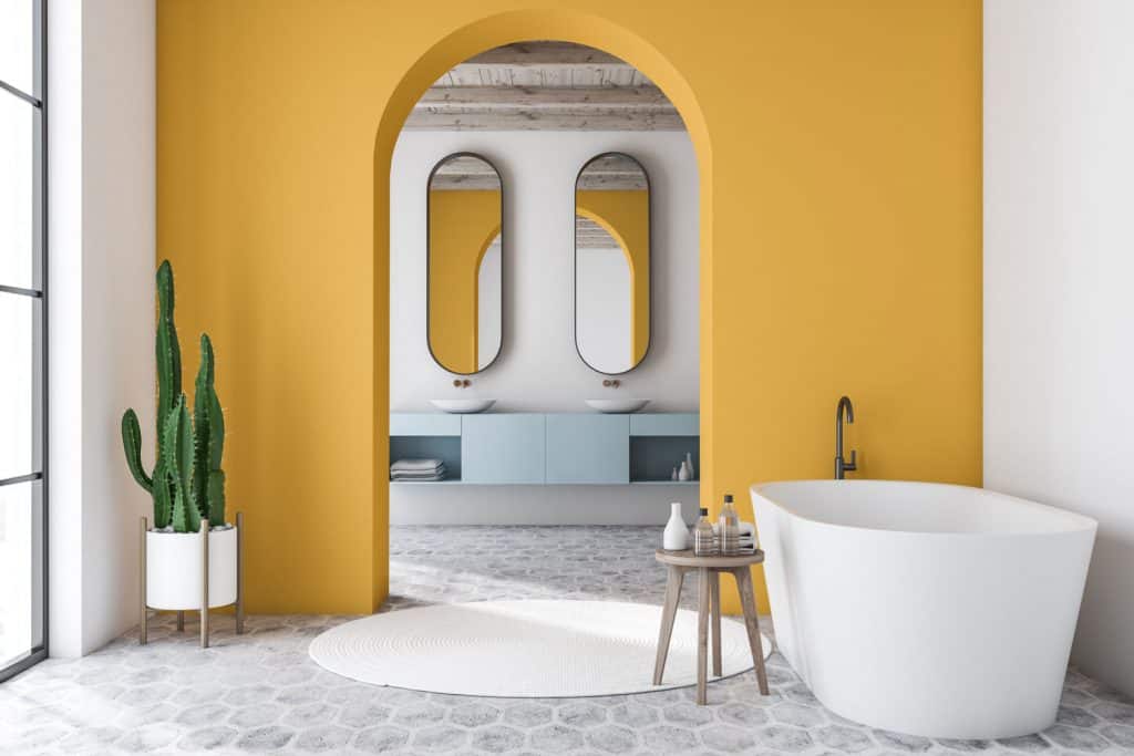 An arched entryway of a bathroom painted in matte yellow and a small bathtub on the side
