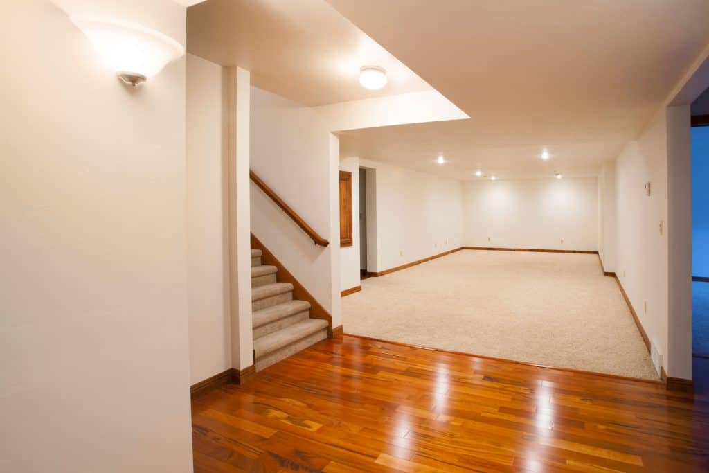 An empty white walled basement flooring with carpeted flooring 
