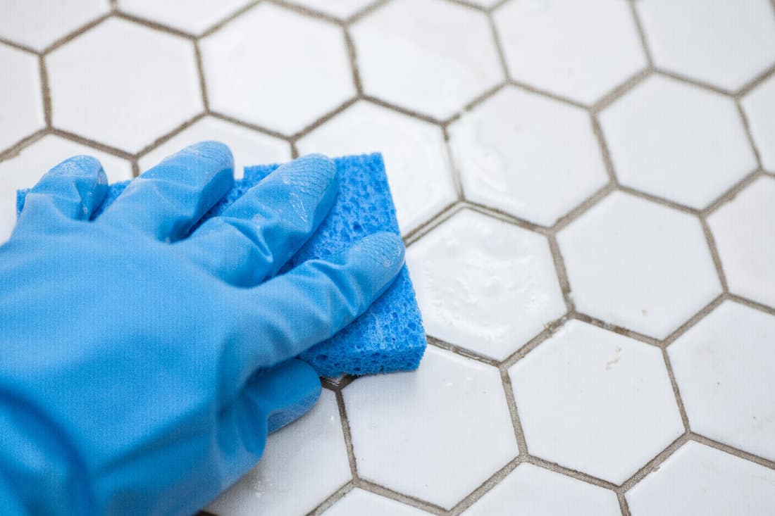 Blue cleaning gloves holding a sponge cleaning a tile floor