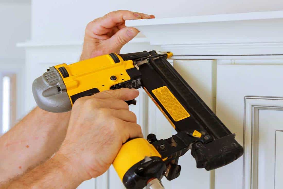 Carpenter brad using nail gun to crown moulding on kitchen cabinets framing trim, How To Nail Crown Molding [4 Steps To Follow]