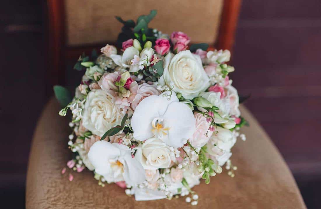 Close up of a wedding bouquet on a vintage chair with orchid and rose